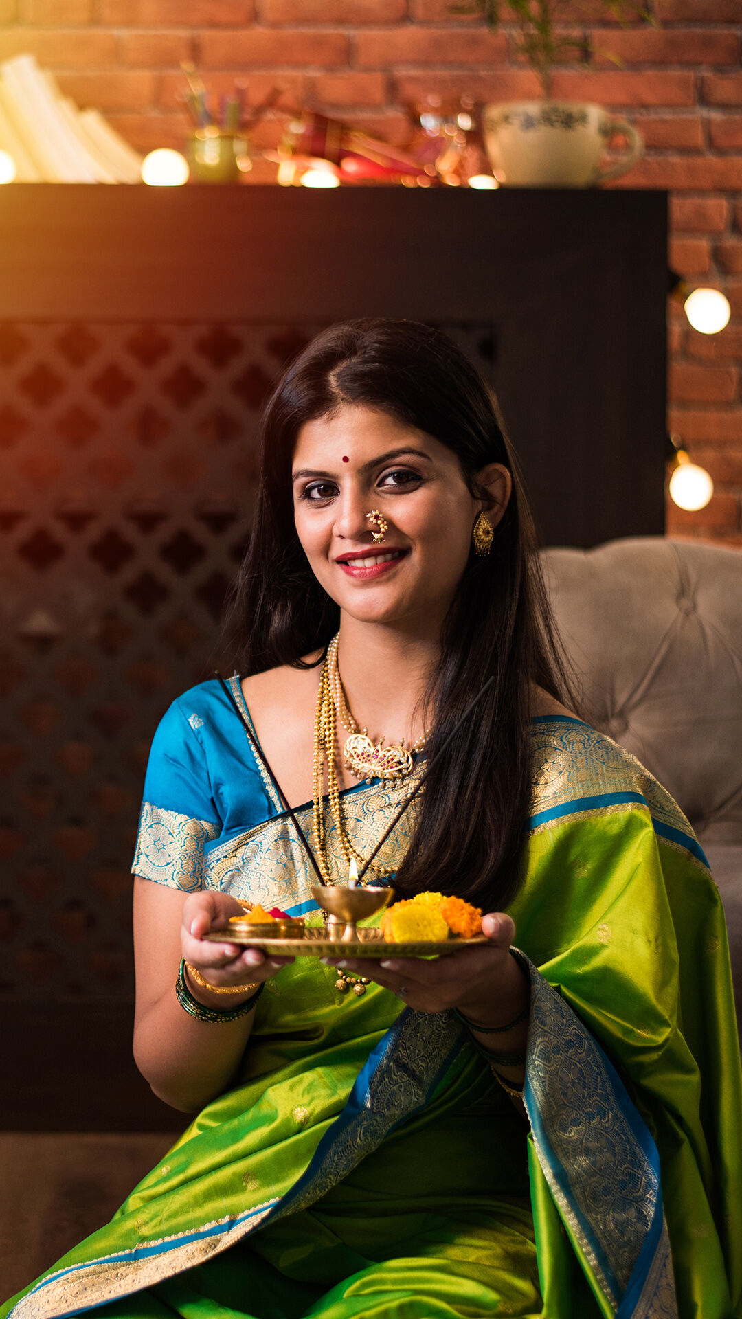 Woman in traditional saree holding decorated pooja thali with diya and flowers during festive celebration